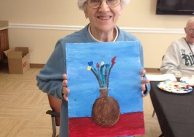Female resident of Park Place of Elmhurst proudly displaying a painting she created